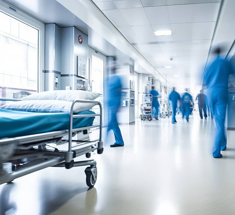 Hospital staff move through a busy healthcare corridor beside a patient bed.