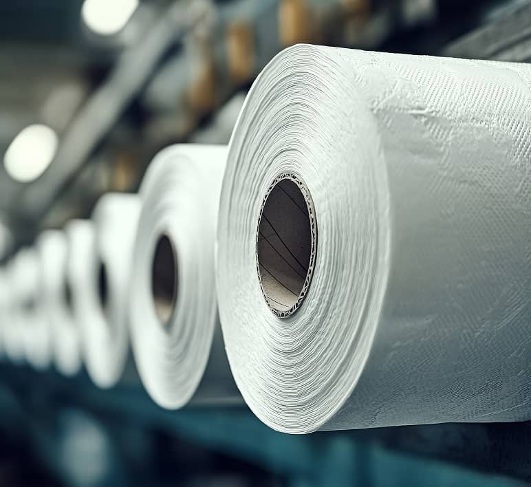 Large rolls of tissue paper are staged in a production facility, representing automation solutions for packaging companies