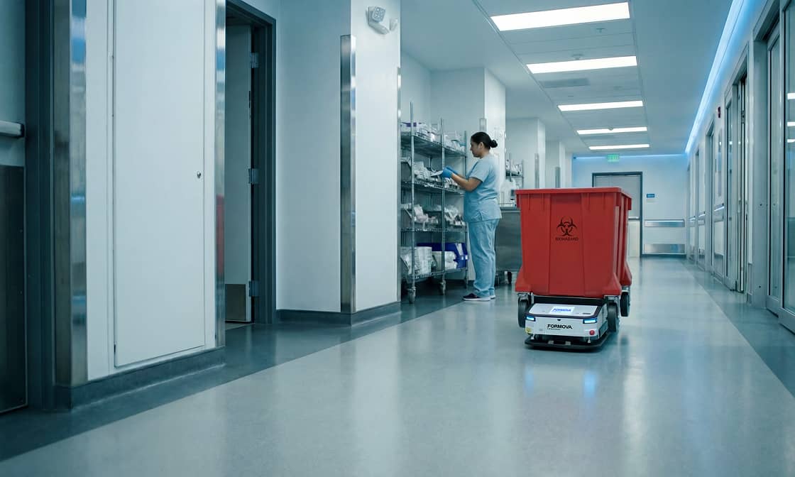 Personnel hospitalier dans un couloir de soins, à côté d'un véhicule automatisé transportant des produits dangereux