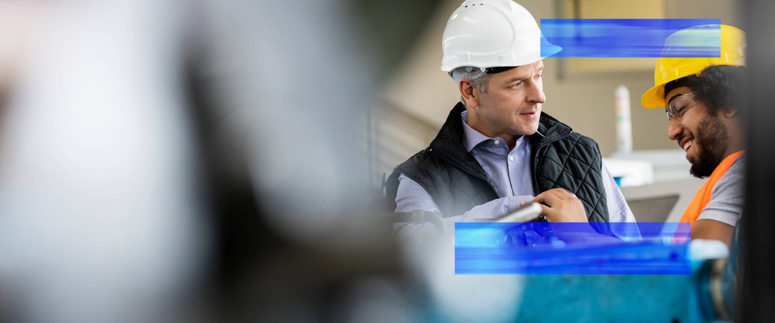Two industrial professionals wearing safety gear collaborate on the production floor