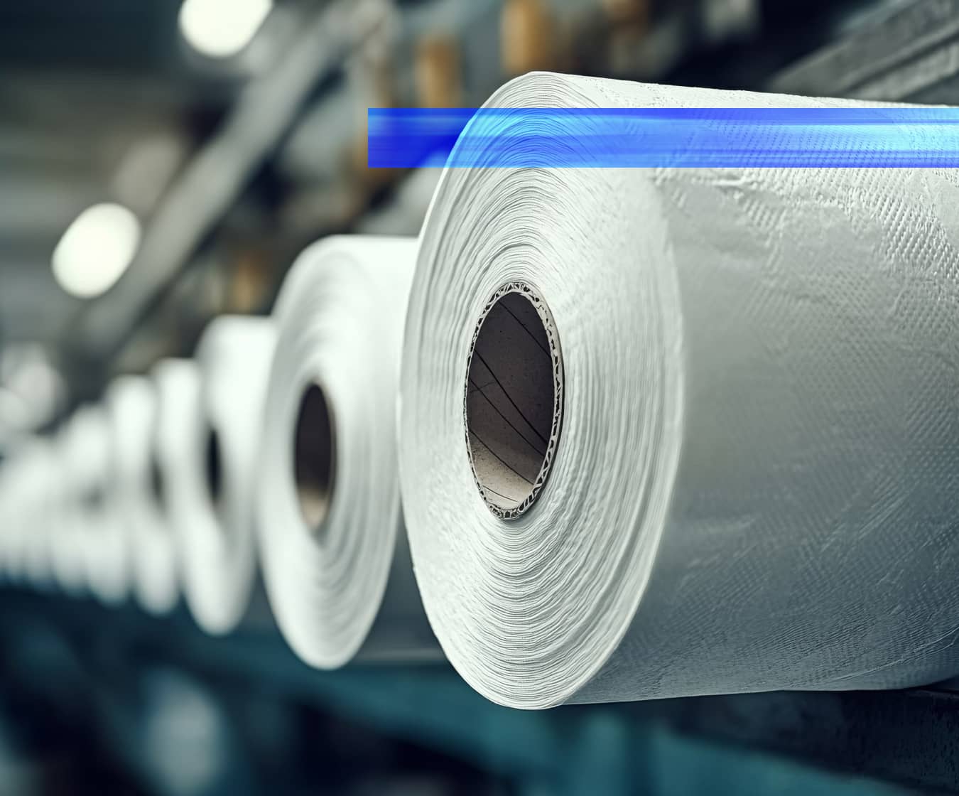 Large rolls of tissue paper are staged in a production facility, representing automation solutions for packaging companies