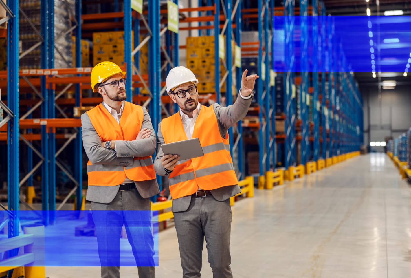 Two warehouse professionals wearing safety gear review operations in a distribution center.