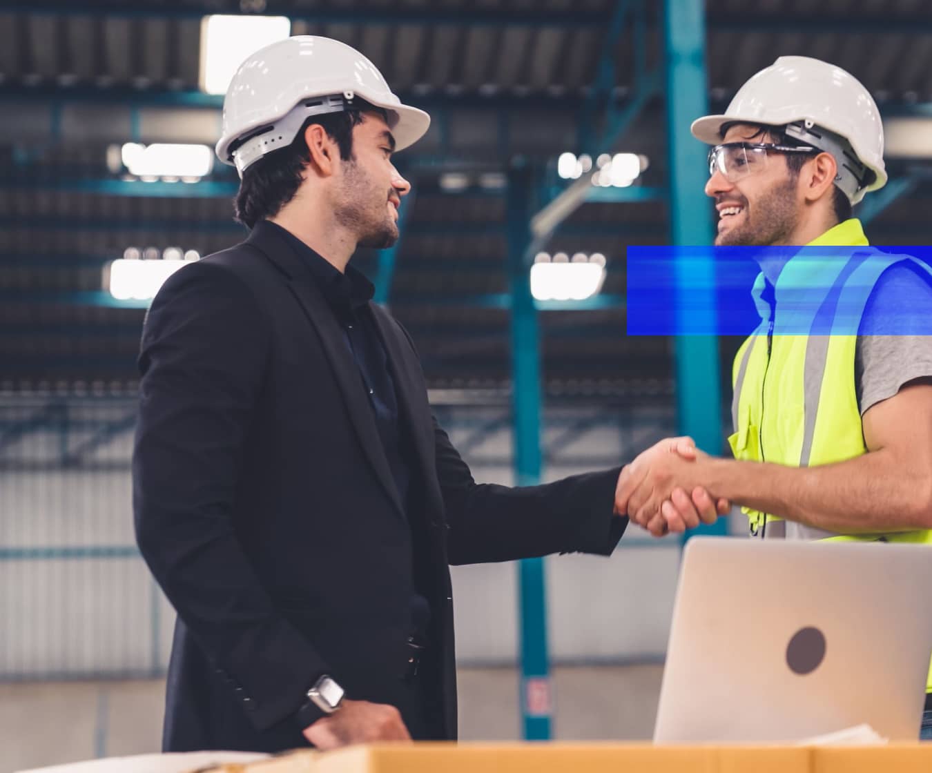 A business leader and industrial operations professional shake hands inside a manufacturing facility