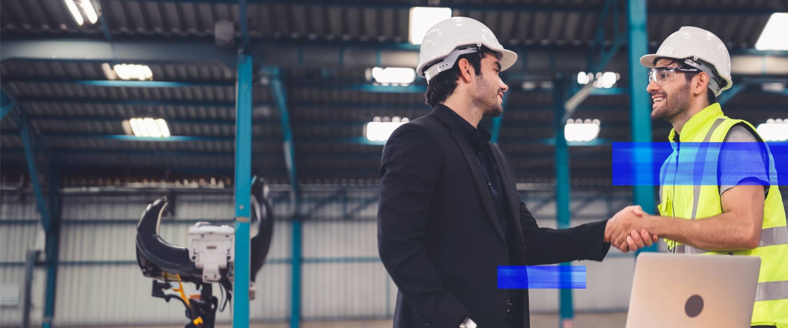 A business leader and industrial operations professional shake hands inside a manufacturing facility